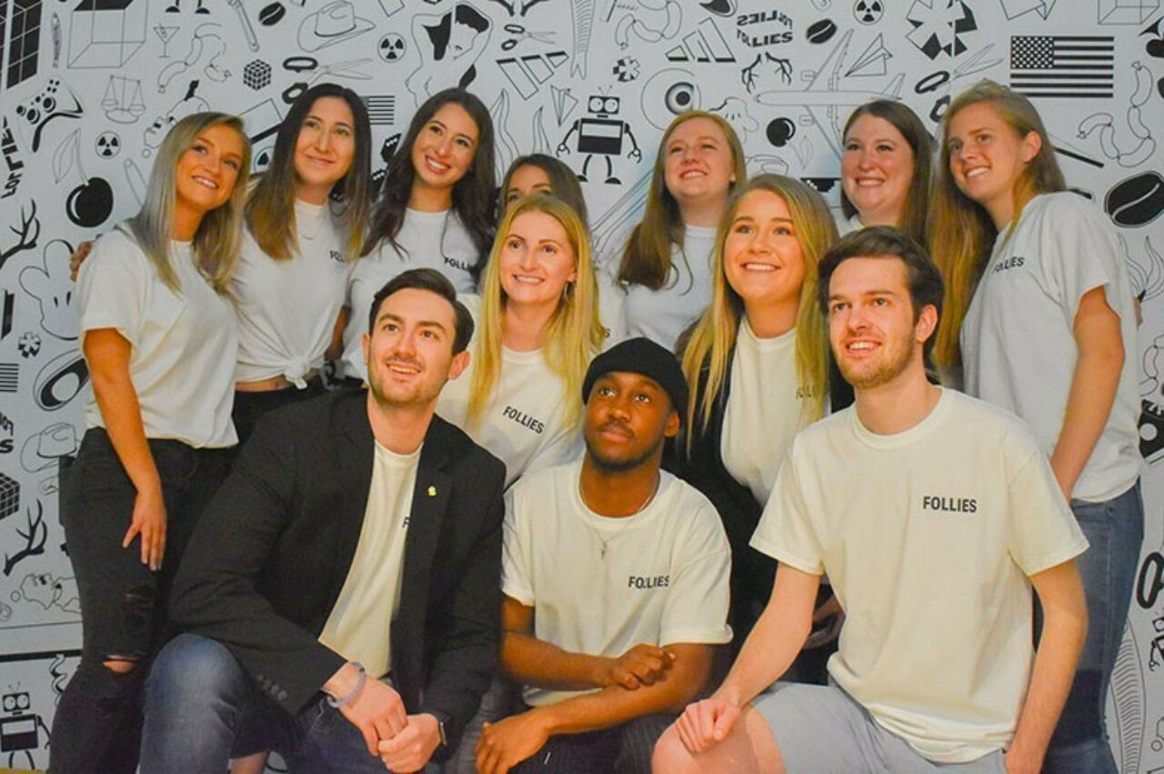 The 19 seniors in the class of 2019 pose in front of a black and white backdrop they designed with icons for the Follies show.