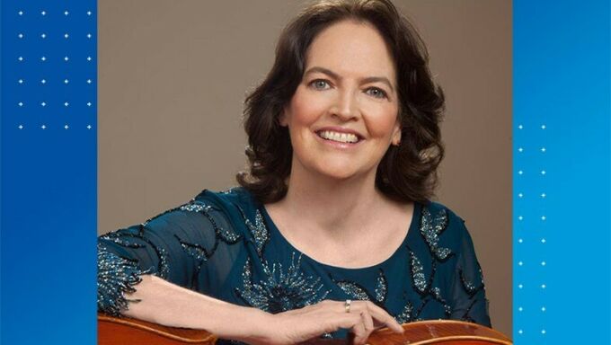 Head shot of a middle-aged woman with brown hair and a green shirt holding a cello