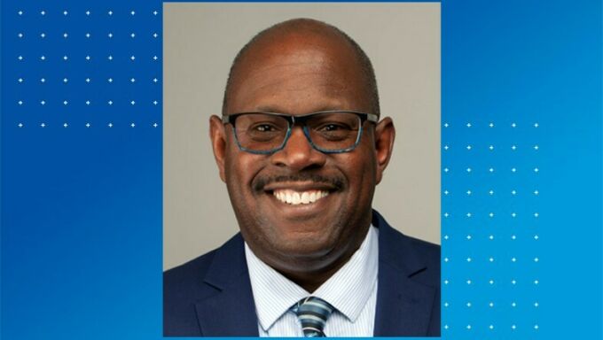 Head shot of a Black man with blue-framed glasses smiling.