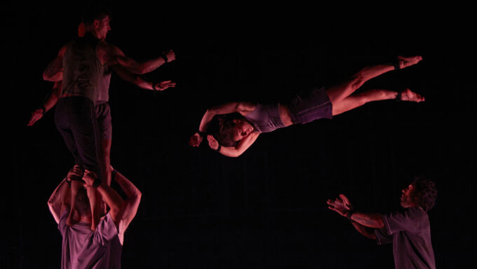 An acrobat stands on a man's shoulders as another does a mid-air flip.