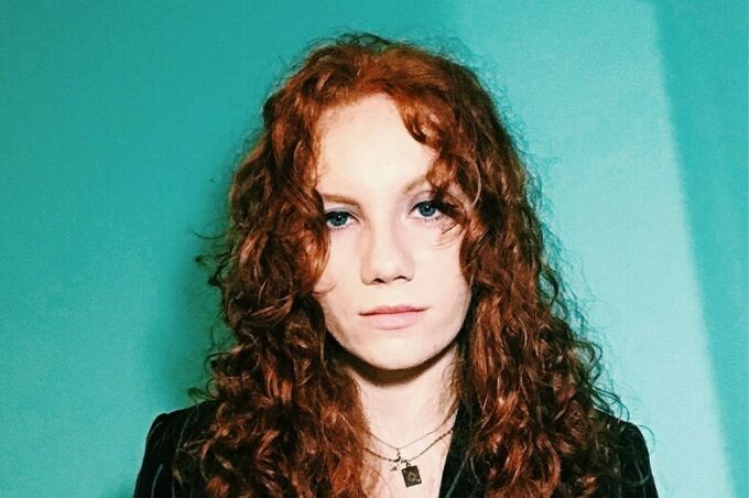 Headshot of a young woman with red hair in front of a teal green background