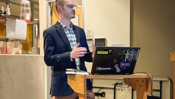 Kieron Cook stands at a podium with an open laptop in front of him.
