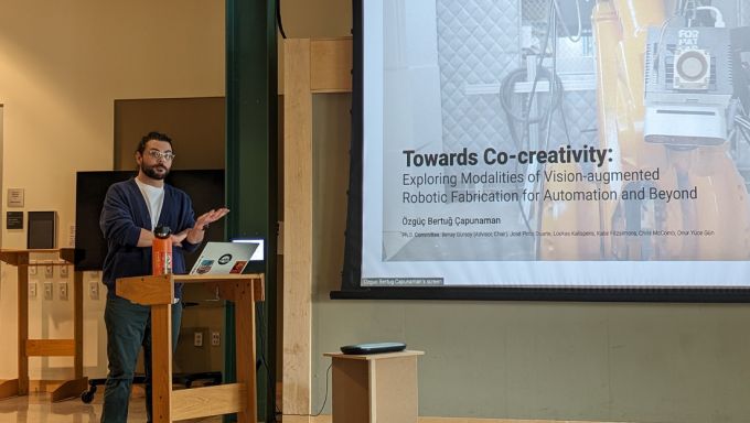 Özgüç Bertuğ Çapunaman standing at the podium in the Stuckeman Family Jury Space while presenting his doctoral thesis.