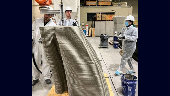 Research lab team members observe a concrete structure being 3D printed.