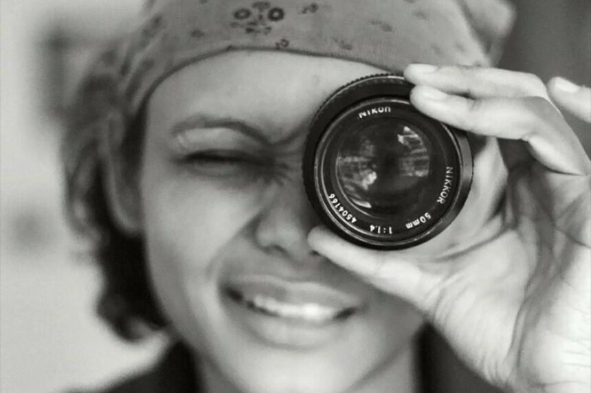 Black and white photo of a woman with short dark hair looking through a camera lens