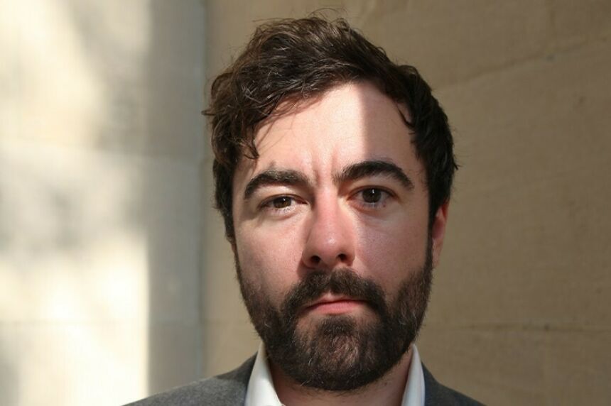 Headshot of a man with short, wavy brown hair and matching beard