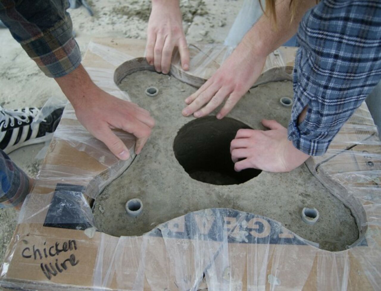 Students' hands working on a wooden and plastic concrete casting mold.
