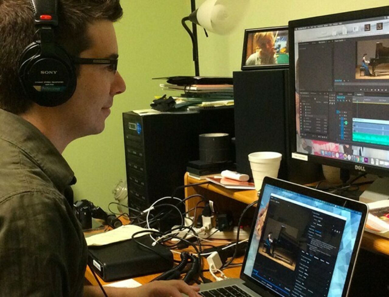Man wearing headphones using a computer with multiple screens to engineer audio tracks for a video clip