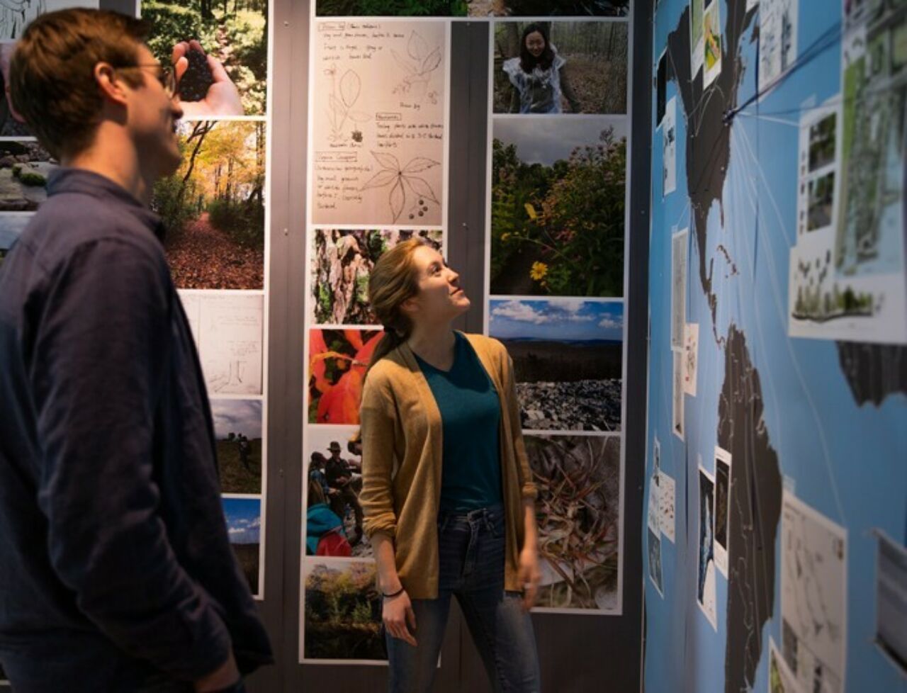 Two students discussing a landscape architecture design project pinned up on wall for review.