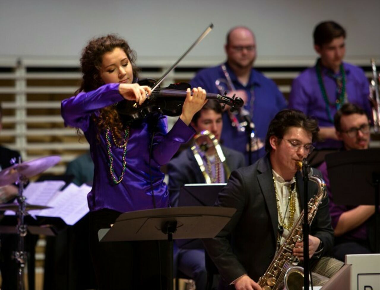 School of Music student playing the violin on stage during the Mardi Gras Jazz Concert at the Recital Hall.