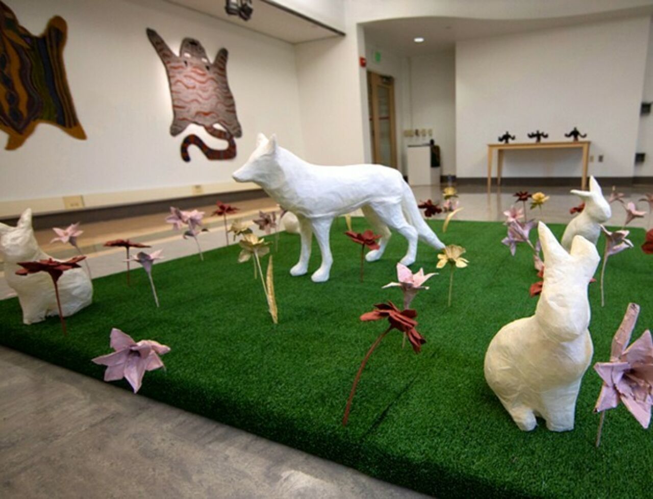 Installation created by Ryan Lawson, showcasing a wolf, rabbit and other animals and colorful flowers on a platform of artificial turf.