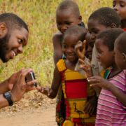 Close-up of Penn State Landscape Architecture student showing a camera to a group of smiling Tanzanian children