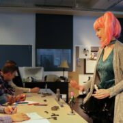 A student presents her 3d model figurine concept to a panel of judges during the Arts Business Ideas Competition. Mimicking the look of her 3d model, she wears a pink ponytail wig and vibrant outfit.