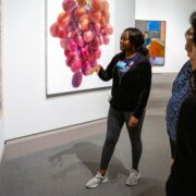 A public collection of late artwork displayed at the Palmer Museum of Art. A student explains the meaning of the piece to visitors.