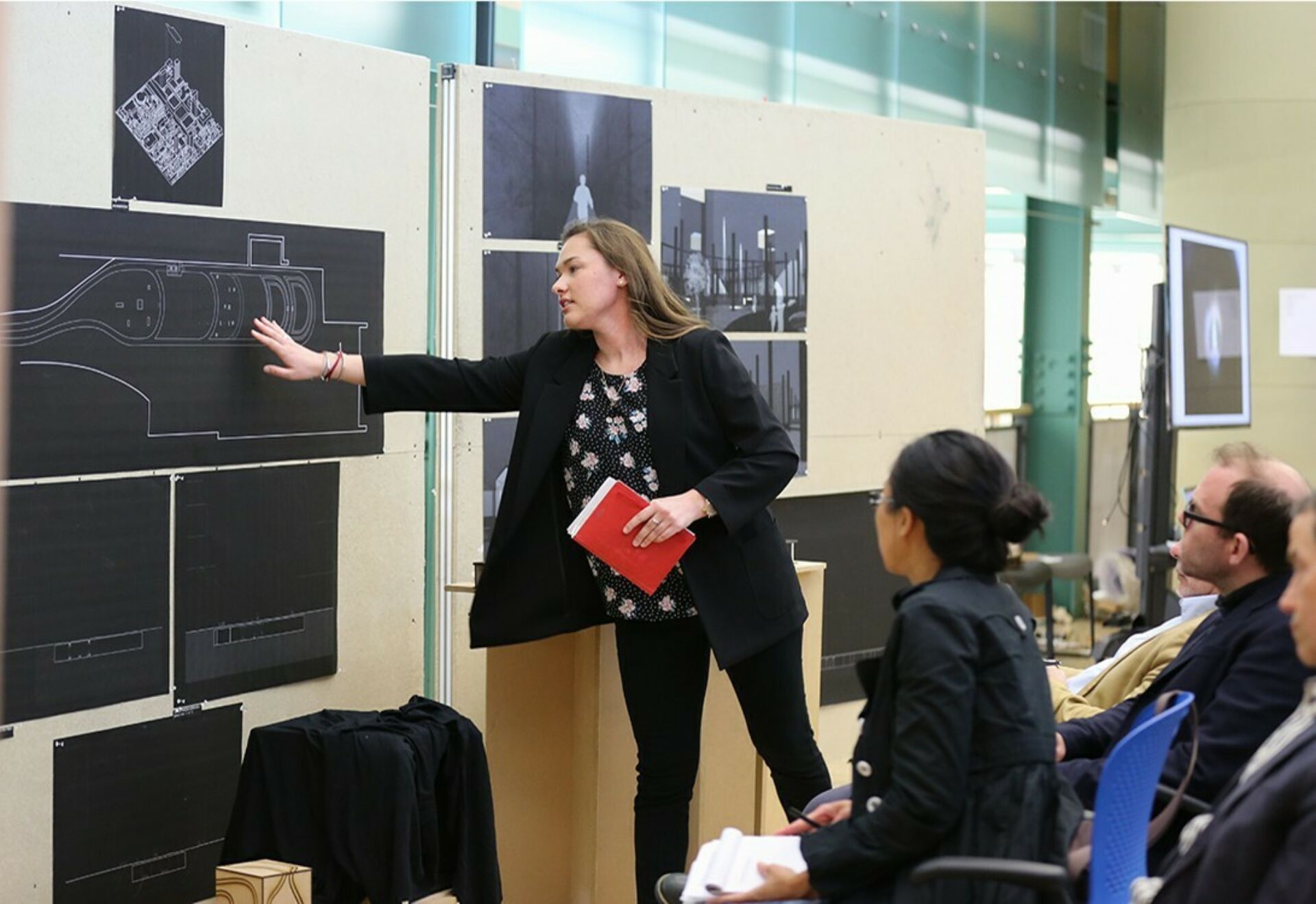 A female architecture presents her pinned up boards during reviews to the jury.