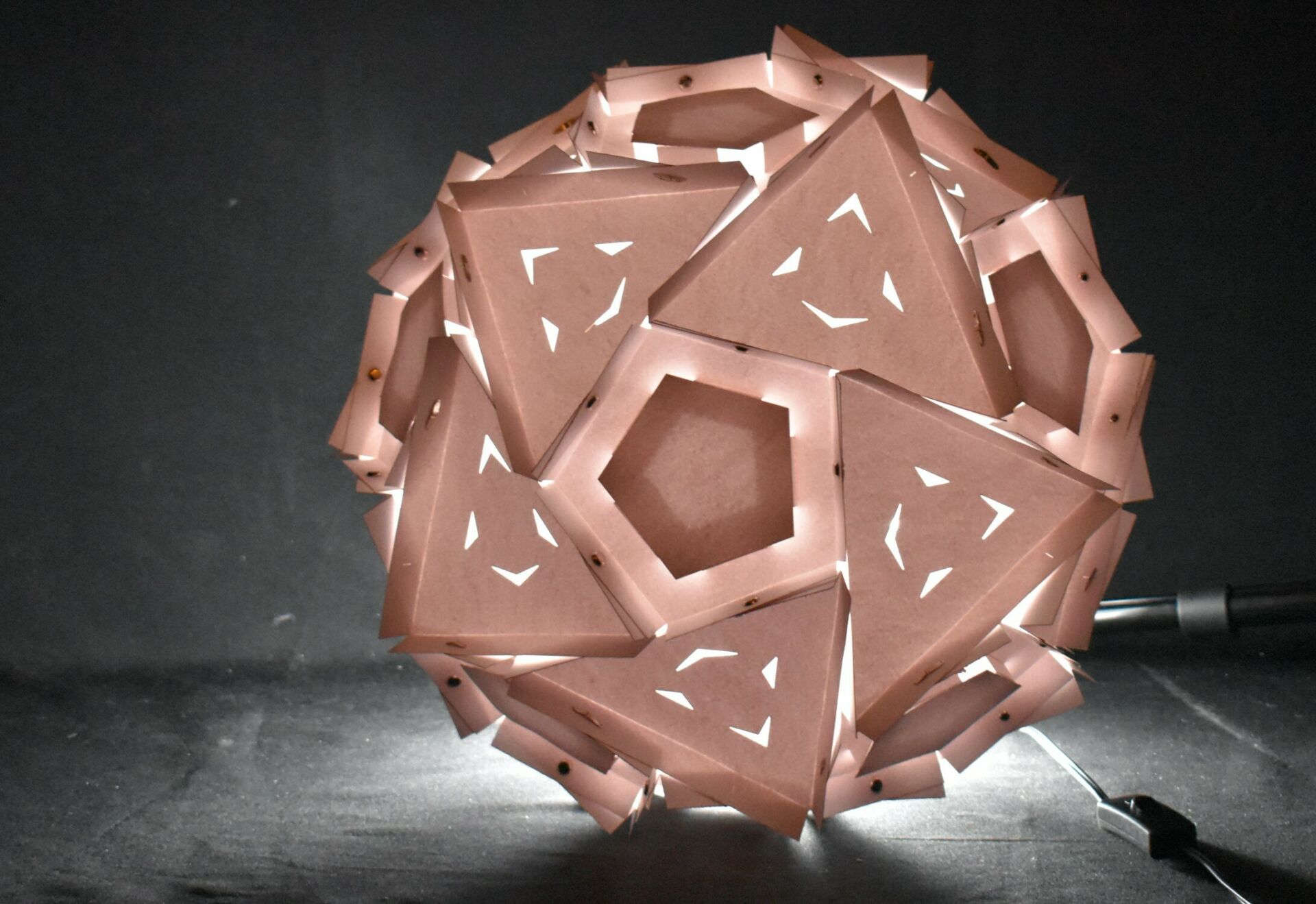 A spherical architectural lantern with light emanating from within a repeating pattern of laser-cut facets.
