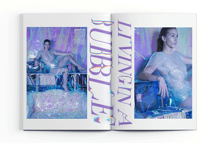 Social Fashion Magazine. Centerfold of a young long haired brunette wearing a short sleeve "blouse" made of bubble wrap. She sits in a poising pose on a low bookshelf with one leg up and arm rested over her knee. The interior of the room is covered with cellophane sheets which gives off iridescent colors highlighting purple. At the center of the fold, large purple text reads: "Living in a Bubble."