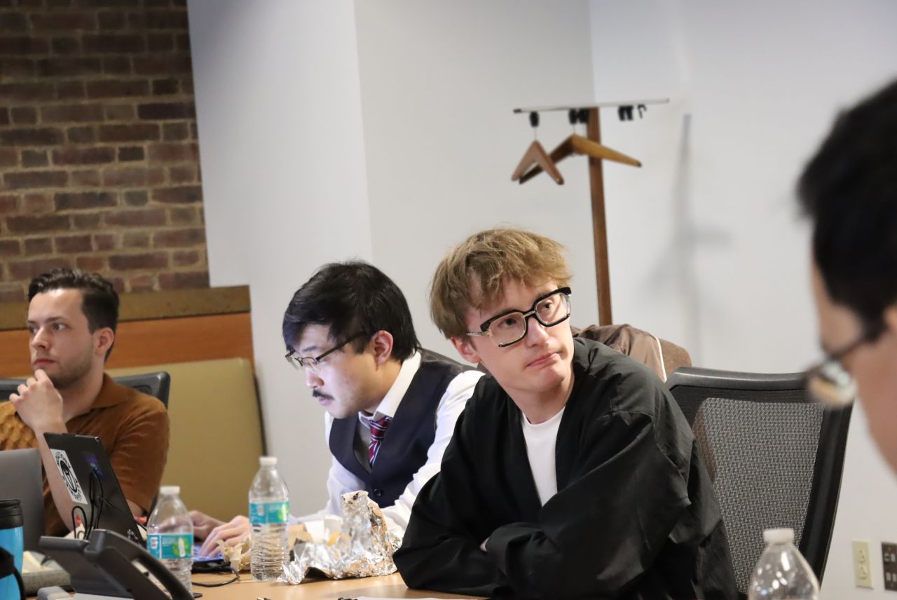 Group of students at table, one student suit jacket turned towards others