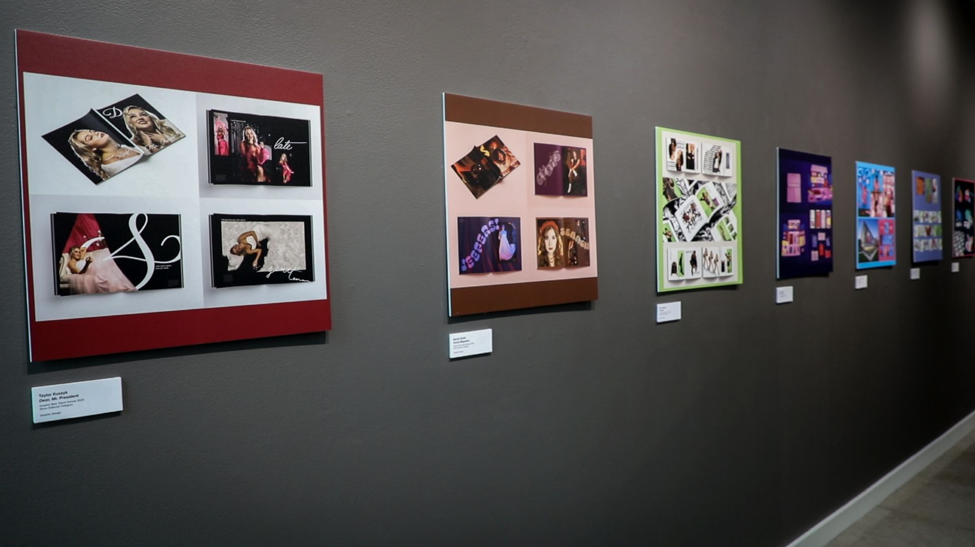 The dark wall of a gallery with a line of images of students work.