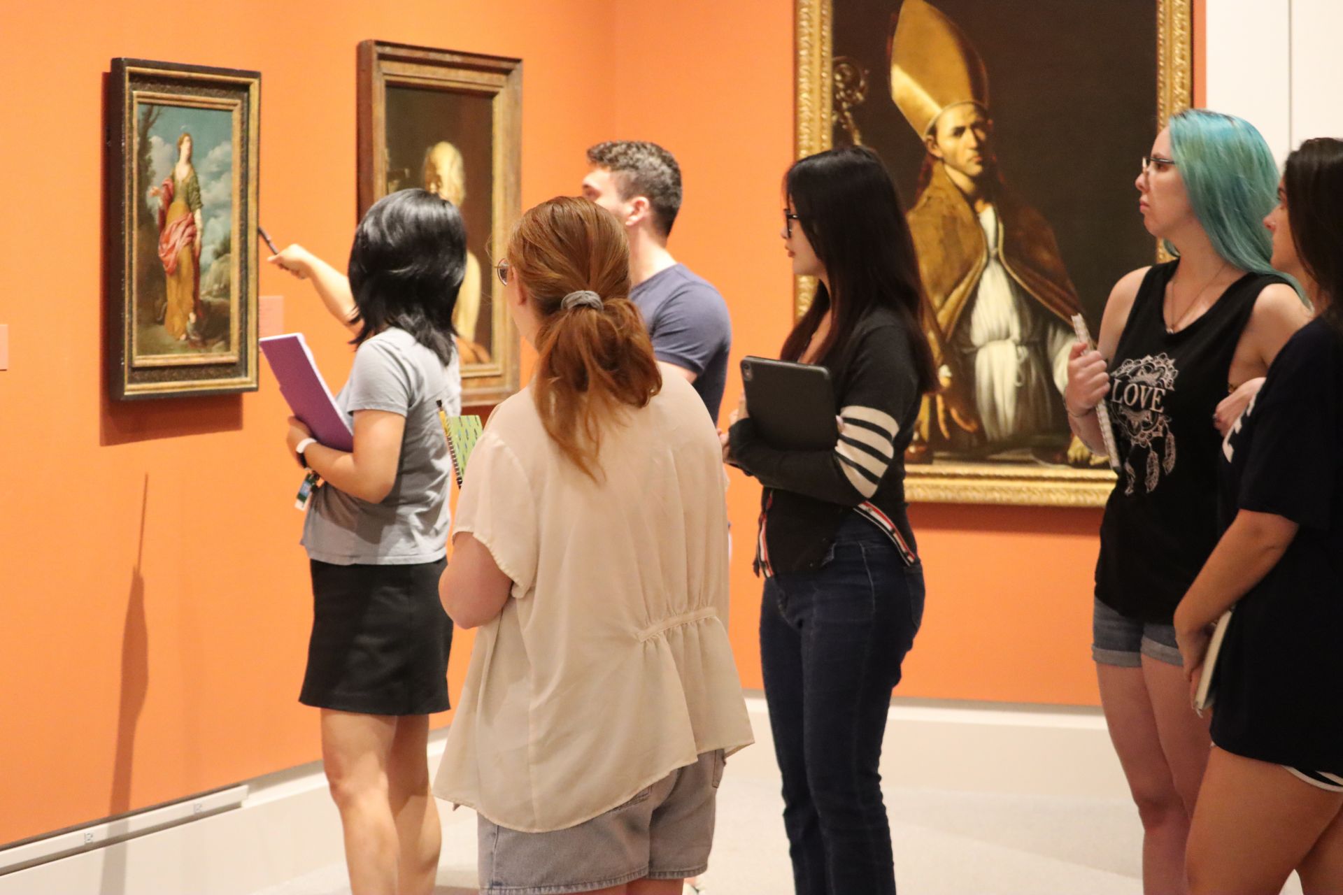Group of students watching as woman points to a painting in the museum