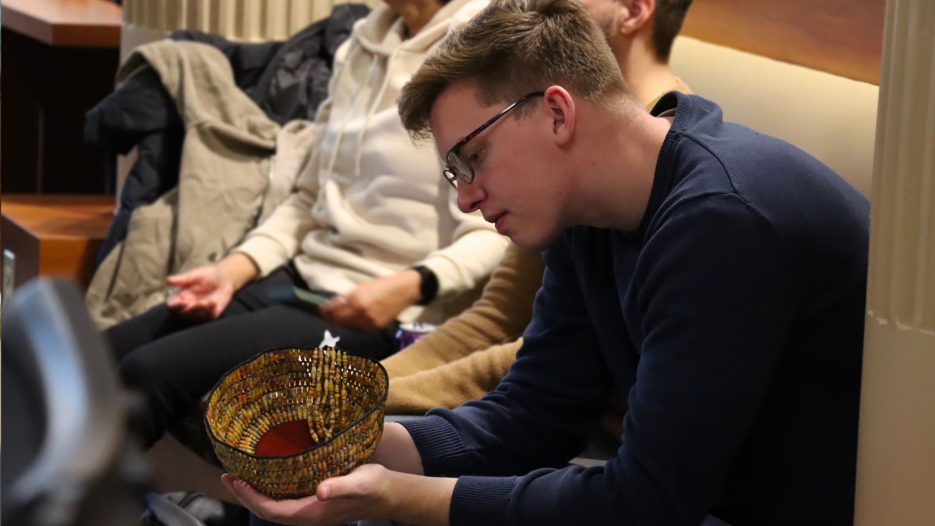 Art History PhD student examining an ornately woven and beaded bowl.