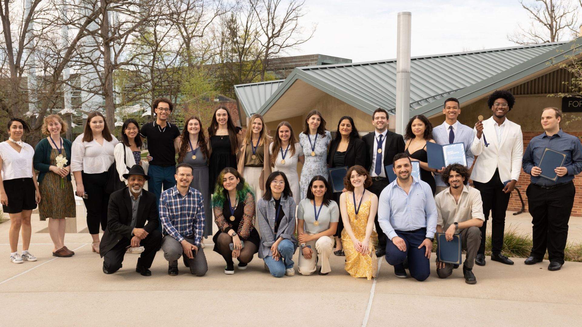 A group of two dozen student award winners and Dean Stephen Carpenter arrayed in two lines – one standing and one kneeling – with Penn State's Forum and Stuckeman Family Building in the background.