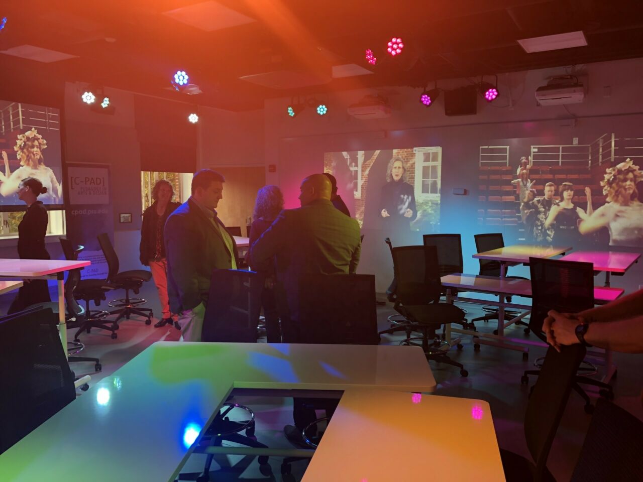 white tables and black desk chairs, people in business wear talking under colorful lights