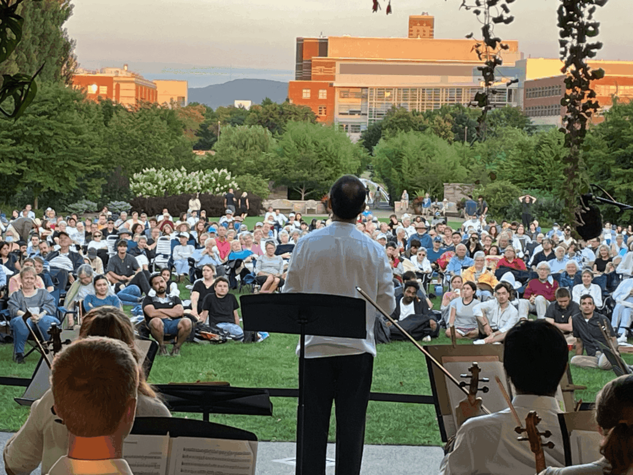 View of an audience outside on a lawn enjoying the sounds of the Penn's Wood Music Festival orchestra.