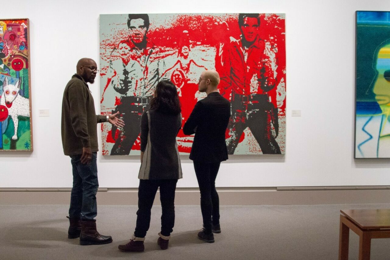 Three people talking in front of large painting in gallery.