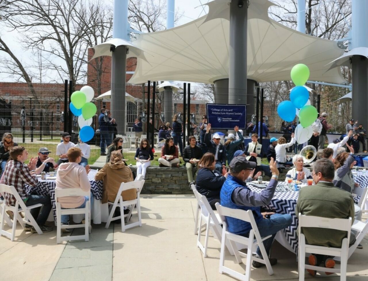 People seated at round tables outdoors with balloon centerpieces.