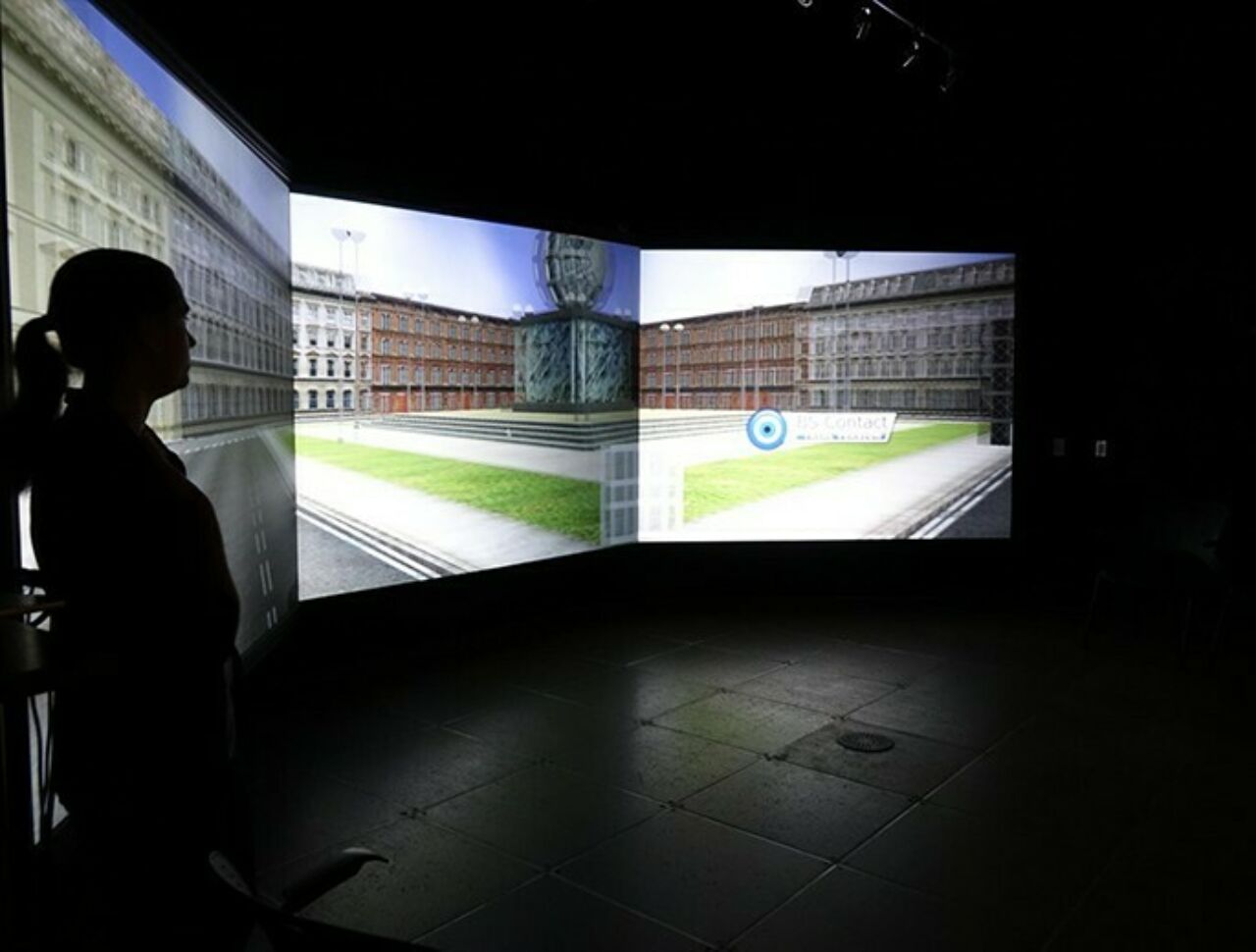 A female student's profile at left against an immersive reality background on a screen behind her in a darkened lab.