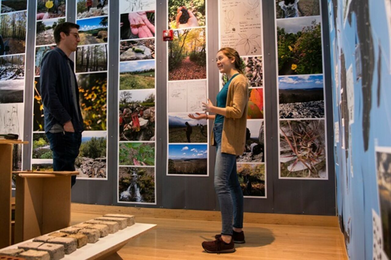 A landscape architect student explaining her many posters and vibrant images displayed on a wall during a landscape architecture student display event.