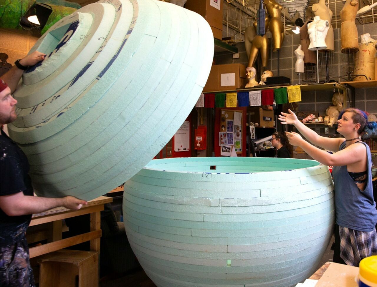 Students adding a cylindrical top to a prop they created out of styrofoam.