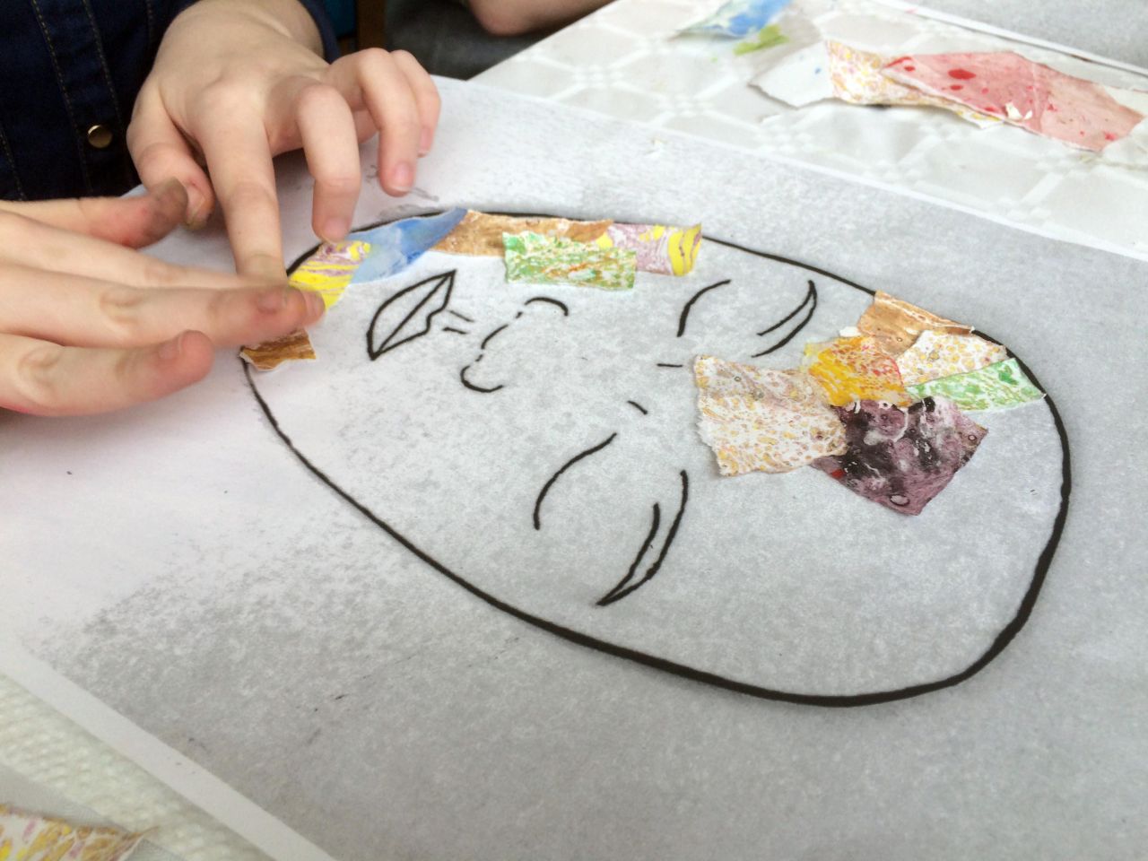 A pair of hands applying scraps of fabric in mixed patterns over an outlined illustration of a human face.