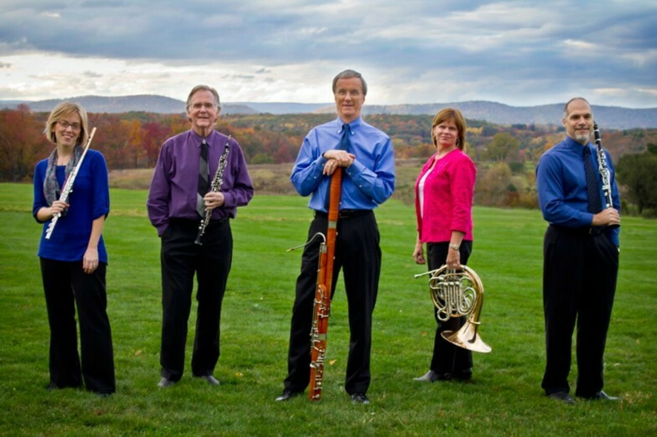 Five Penn State Music faculty members who make up the Pennsylvania Quintet, posing in a green, grassy field with moody mountains and sky in the background.