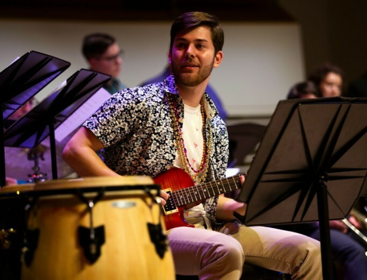 School of Music student playing the guitar on stage during the Mardi Gras Jazz Concert at the Recital Hall.