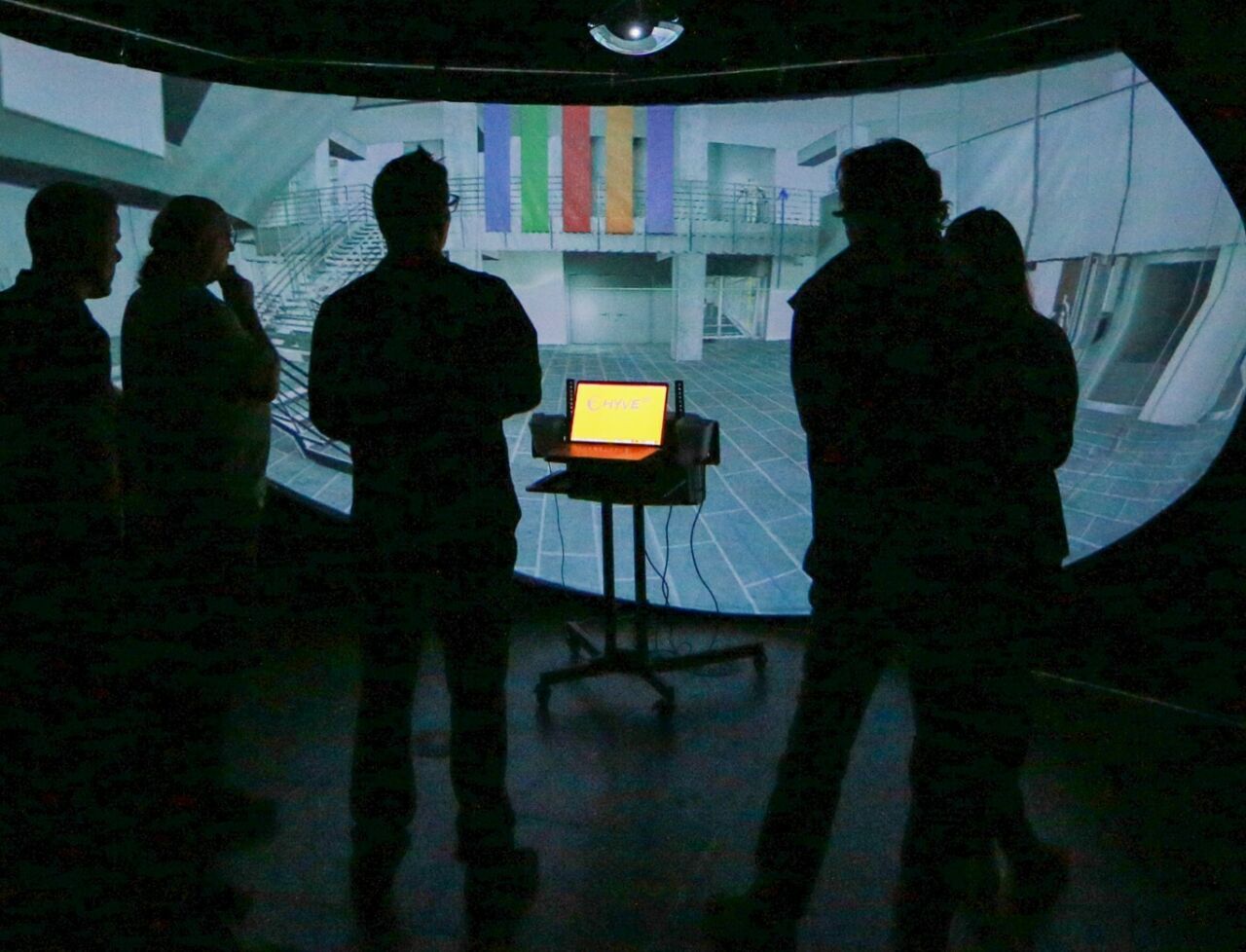 A group of researchers standing in a darkened room engaging with a virtual environment projection