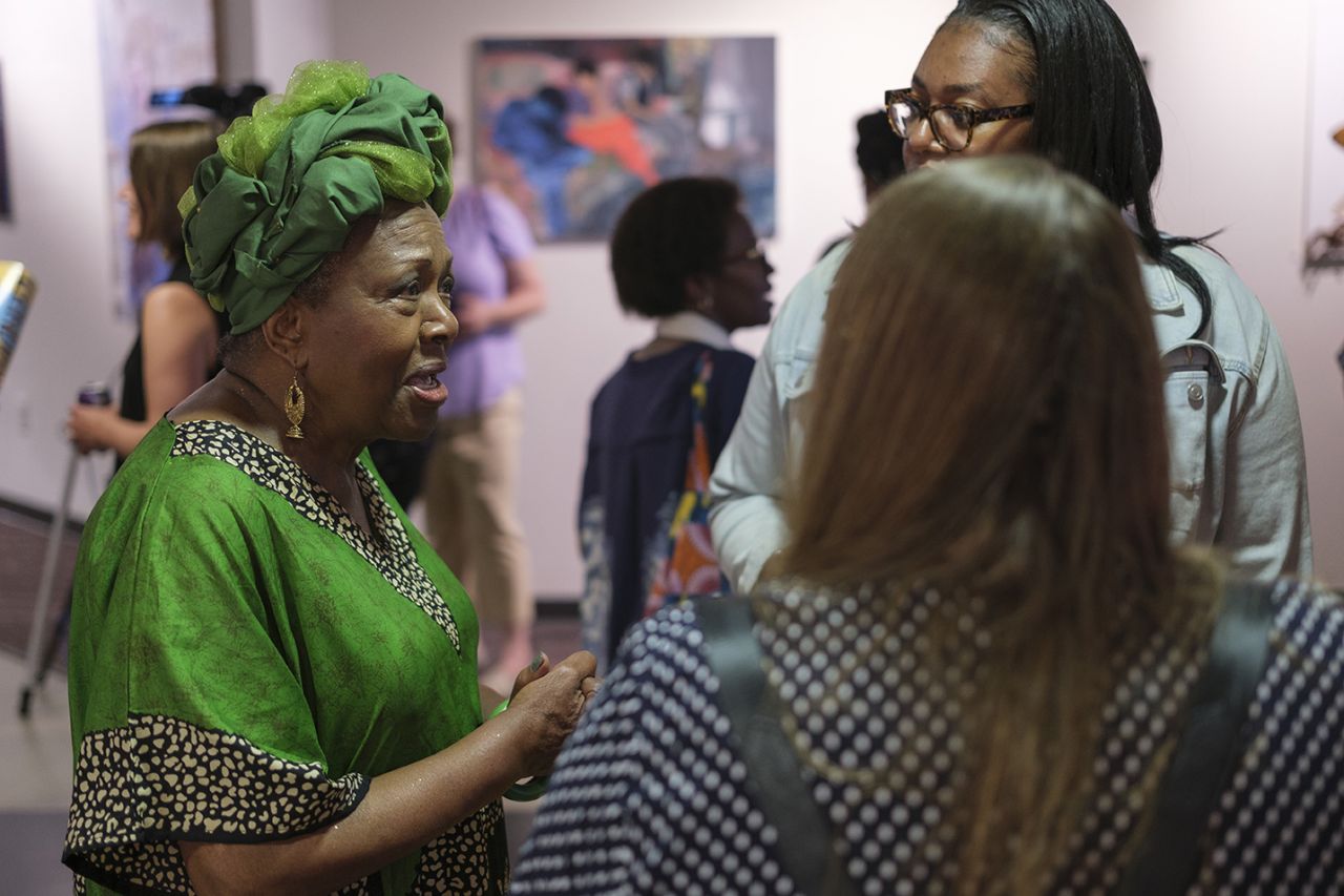 A Black woman in traditional African clothing conversing with two other women.