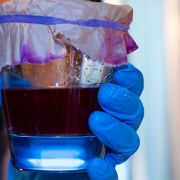 Red dye in clear glass held by blue gloved hand