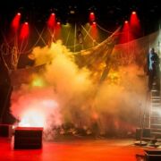 Dramatic stage and lighting design for the play Albatross. A red cast of light permeates the stage with clouds of white smoke surrounding the actor standing on top of a tall ladder.