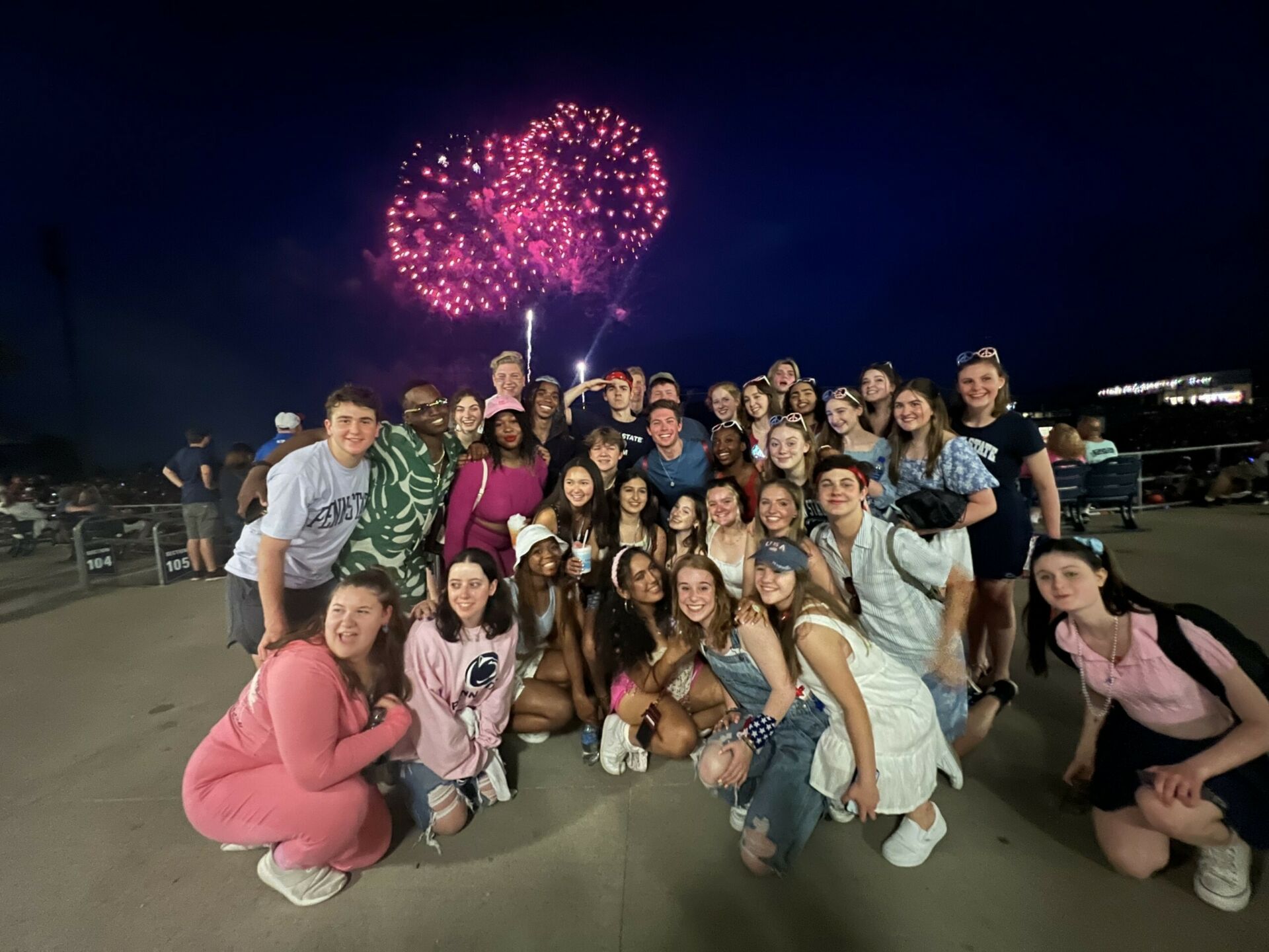 group of students pose for a photo at July 4 celebration with fireworks in night sky
