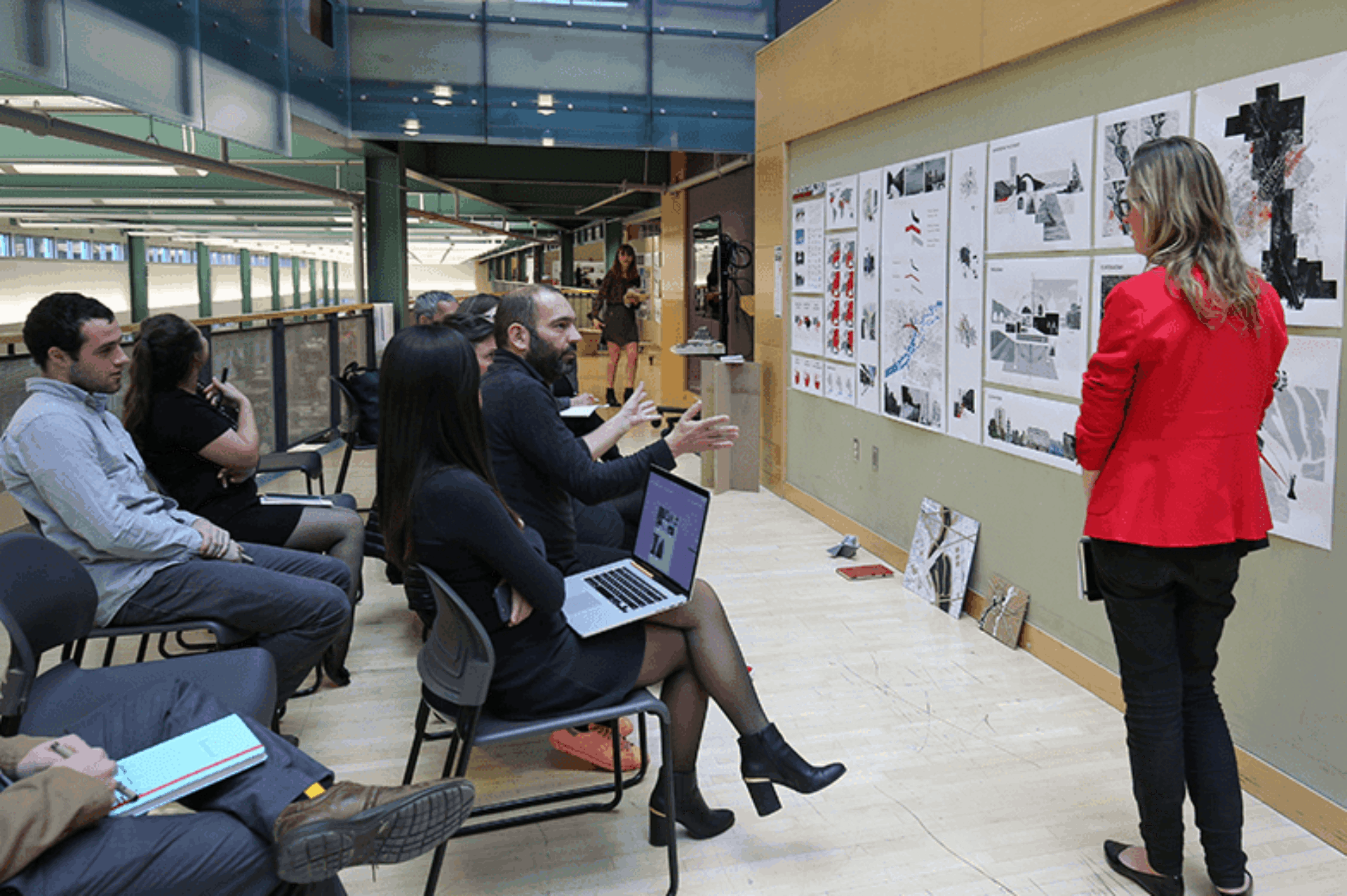 An architecture student standing in front of her project on a pin-up board, listening to the critique of a professor.