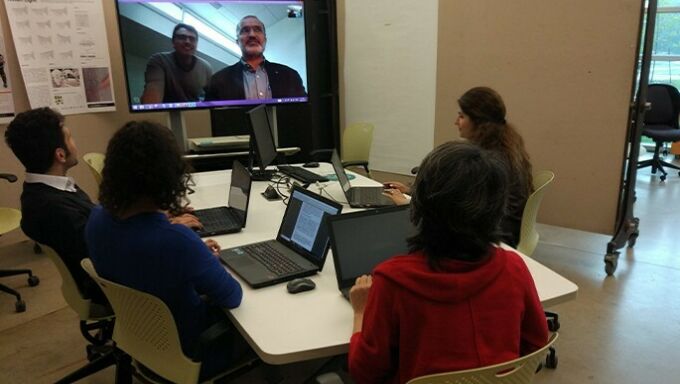 Students sitting around a conference table videoconferencing with a researcher.