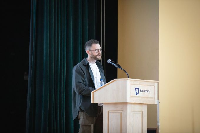 A man with glasses stands behind a podium with a microphone