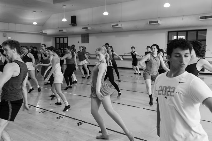 Black and white photo of a group of theatre camp dancers in studio moving forward in sync with their left leg and left arm out to their side.