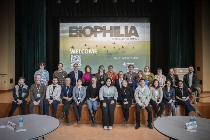 A group of people in front of a screen projected with the conference welcome sign.