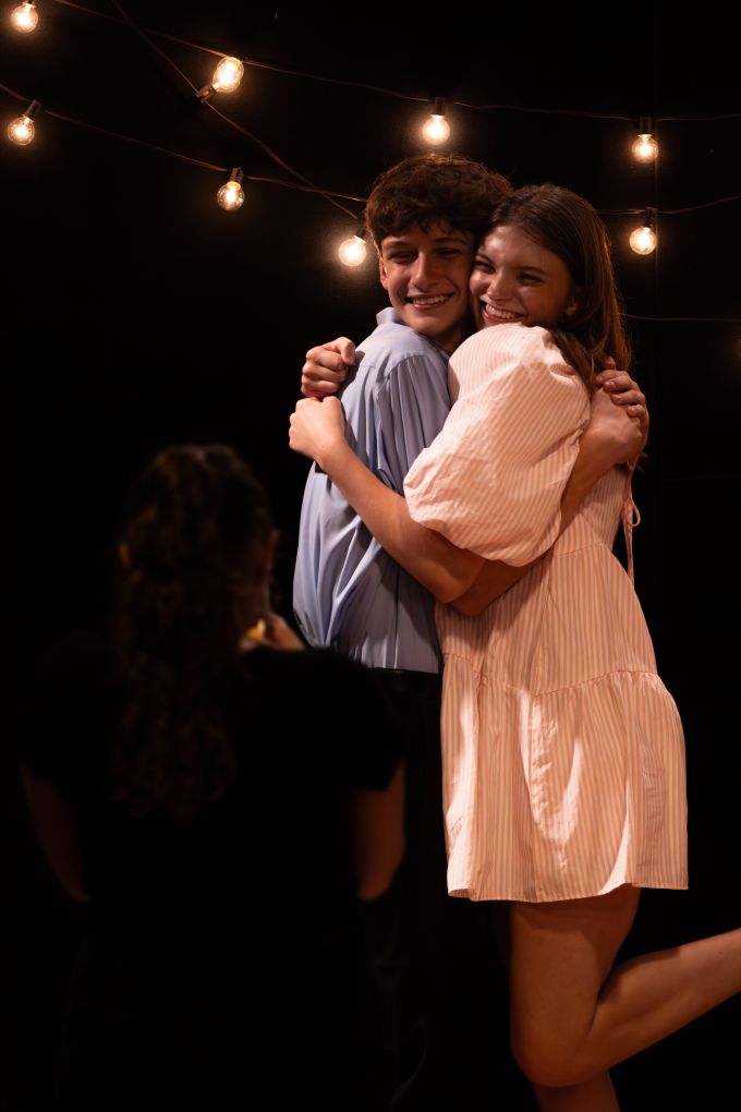 A theatre camp male and female smiling hugging on stage after a performance.