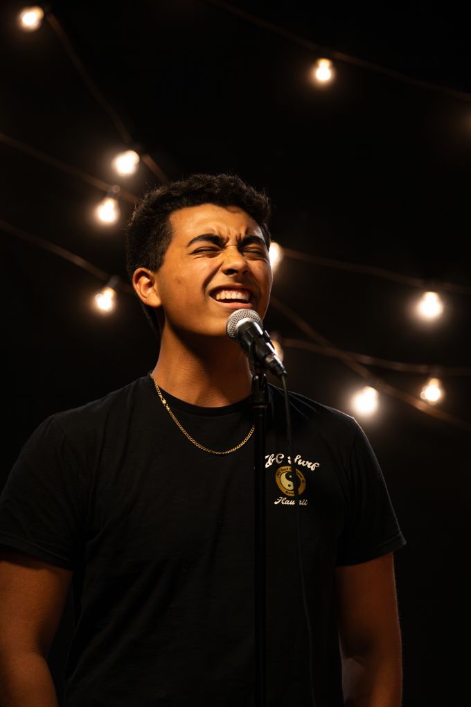 Individual male theatre camp student singing a song into a microphone with eyes closed.