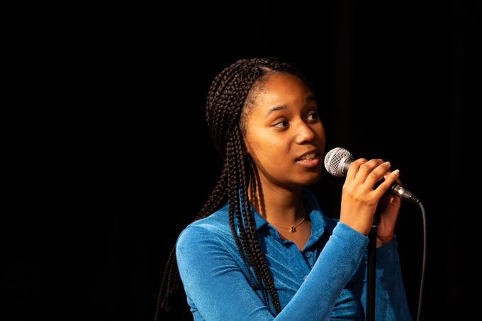 Individual theatre camp female with her hands around a microphone singing into the distance.