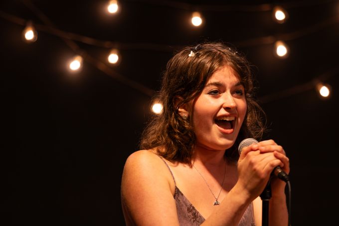 Individual theatre camp female singing into a microphone with pure joy on her face.